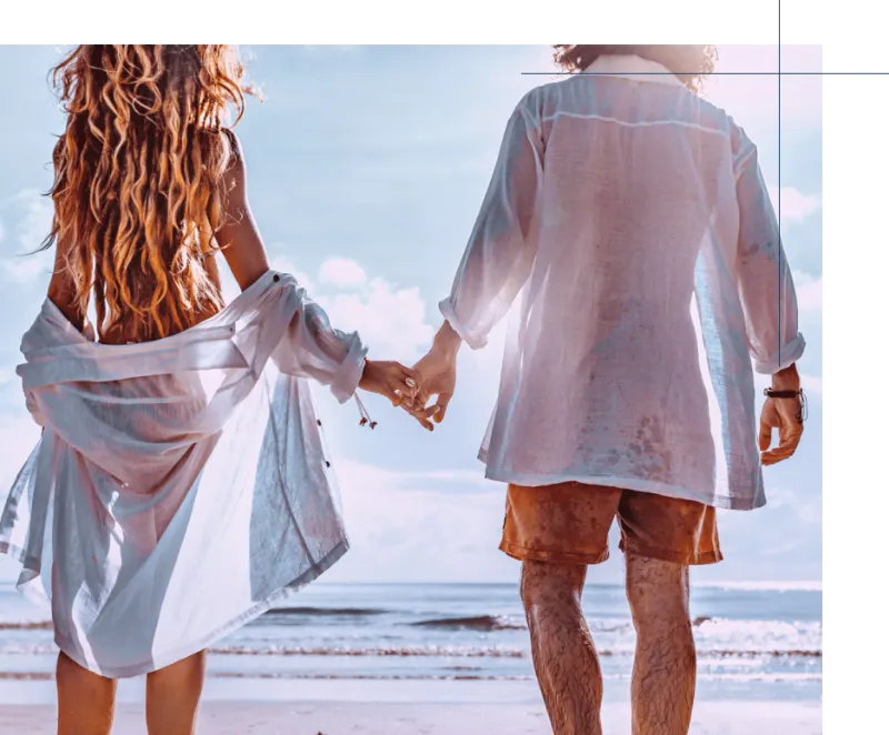 A couple holding hands as they walk toward the ocean